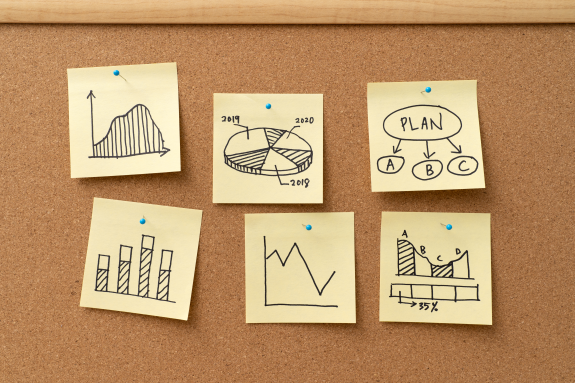 Cork board with hand-drawn charts and diagrams on sticky notes.