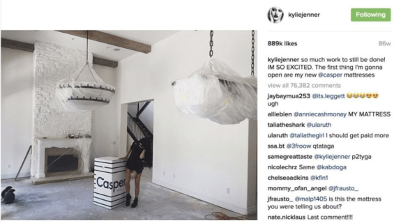 Woman standing next to a Casper mattress box in a living room with covered chandeliers.